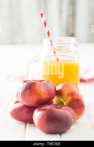 Ripe flat nectarines and juice glass on white table. Stock Photo