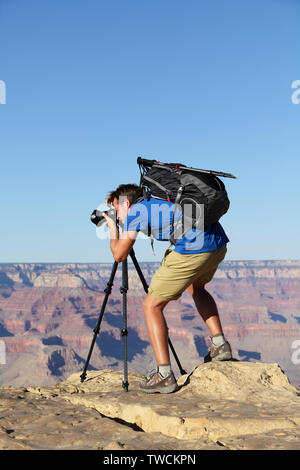 Nature landscape photographer in Grand Canyon taking picture photos with SLR camera and tripod during hike on south rim. Young man hiker enjoying landscape in Grand Canyon, Arizona, USA. Stock Photo