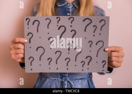 Woman holding paper with question marks while standing in front of the wall. Stock Photo