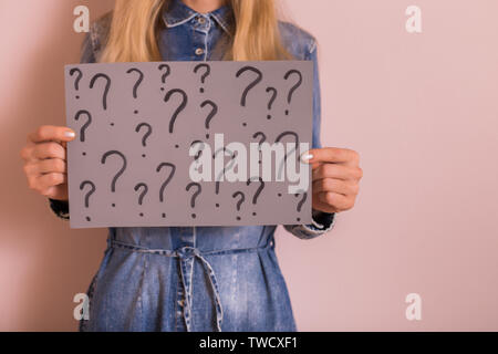 Woman holding paper with question marks while standing in front of the wall. Stock Photo