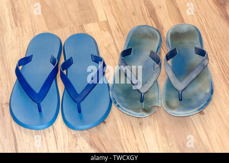 New and old dirty flip flops on light brown floor. Two pairs new and worn out shoes. Blue sandals isolated on wood background. Before and after concep Stock Photo