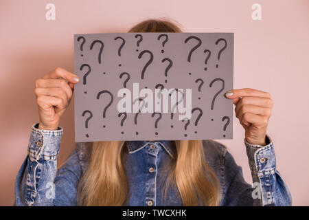 Woman holding paper with question marks while standing in front of the wall. Stock Photo
