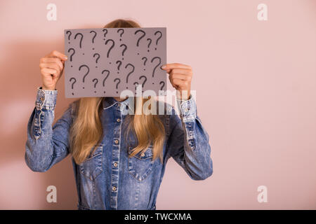Woman holding paper with question marks while standing in front of the wall. Stock Photo
