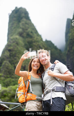 Couple taking selfie self portrait hiking on Hawaii in outdoor activity. Woman and man hiker taking photo with smart phone camera. Healthy lifestyle from Iao Valley State Park, Wailuku, Maui, USA. Stock Photo