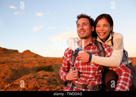 Happy couple active lifestyle hiking enjoying outdoors activity. Smiling laughing young lovers embracing looking at sunset during hike. Cheerful interracial couple, Asian woman, Caucasian man. Stock Photo