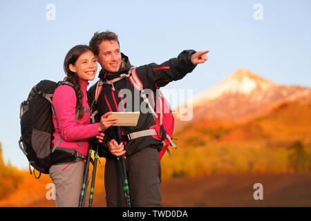 Tablet PC - hiking couple using travel app or map on hike. Man and woman hikers looking at view pointing and showing during hike on volcano Teide, Tenerife, Canary Islands, Spain. Stock Photo