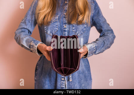 Woman holding empty wallet while standing in front of the wall. Stock Photo