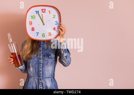 Woman holding alcohol and clock in front of the wall.Quitting drinking alcohol concept. Stock Photo