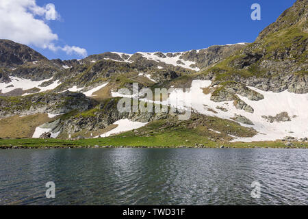 Amazing view across the Kidney lake of large, distant group of hikers climbing up the snow covered hill on a track of famous seven Rila lakes Stock Photo