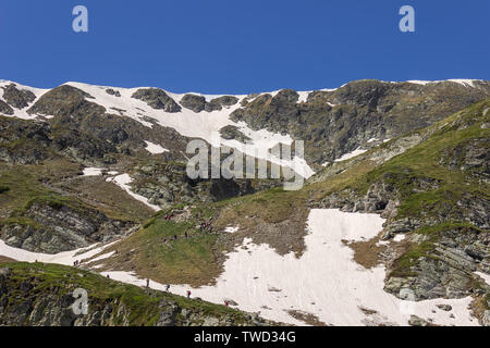 Large group of hikers climbing up the snow covered hill on a track of famous seven Rila lakes in Bulgaria on a sunny day Stock Photo