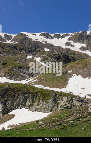 Large group of hikers climbing up the snow covered hill on a track of famous seven Rila lakes in Bulgaria on a sunny day Stock Photo