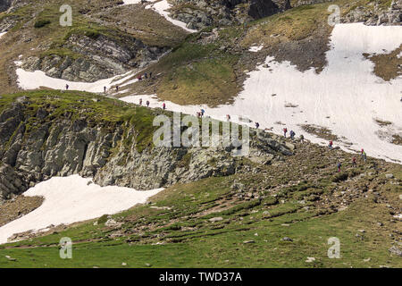 Large group of hikers climbing up the snow covered hill on a track of famous seven Rila lakes in Bulgaria on a sunny day Stock Photo