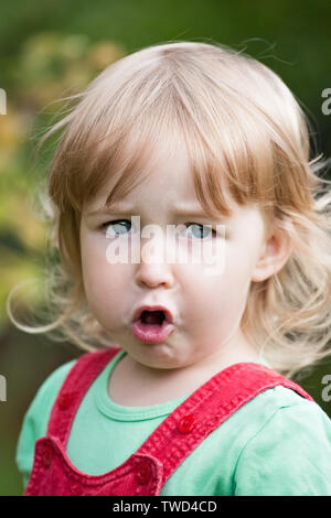 closeup face portrait of chewing cute two years old blonde white girl on summer outdoor background Stock Photo