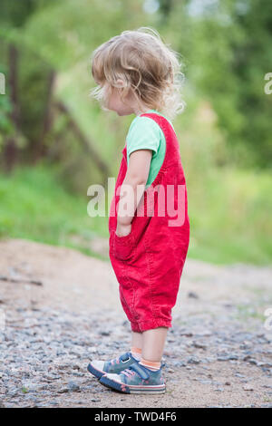 cute kid girl in red pants standing tall on summer outdoor background Stock Photo