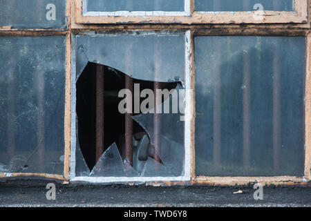 Close-up of smashed and broken rectangular glass window pane set in metal frame of window of service building at Didcot Railway Centre, Oxfordshire UK Stock Photo