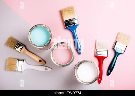 Three open cans of pastel paint with five brushes on pink and grey background. Renovation concept. Stock Photo