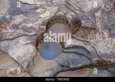 Mysterious circular hole in the red coastal rocks. Stock Photo
