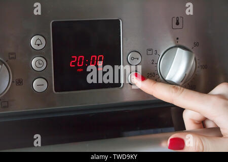 A womans hand puts on the oven a time of 20 minutes and a temperature of 180 degrees for making apple pie, copyspace Stock Photo