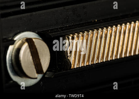 A Brass Linear Gear assembly in Macro.  The black metal plates around it forming the body of the machinery are very dirty and scratched from wear Stock Photo