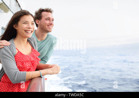 Cruise ship couple romantic on boat looking at view in romance. Happy lovers, woman and man traveling on vacation travel sailing on open sea ocean. Young Asian woman and Caucasian man. Stock Photo