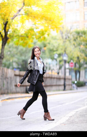 Fashion urban young woman living city lifestyle walking in leather jacket crossing streets in full length in autumn fall. Trendy modern female. Multiracial Asian Caucasian model.
