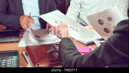 Asian businessmen and businesswomen analysis documents on office table with laptop computer and graph financial diagram working in the background Stock Photo