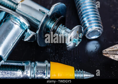 A Macro Image of Drywall Anchors, Screws and Fasteners on a wooden surface with the tip of a screwdriver just in frame from the right Stock Photo