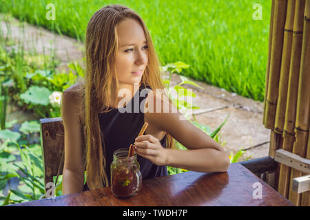 Young woman drinking cold tea with cinnamon in rice field Stock Photo