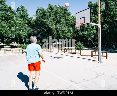 Old man playing and coaching basket alone in a basketball court Stock Photo