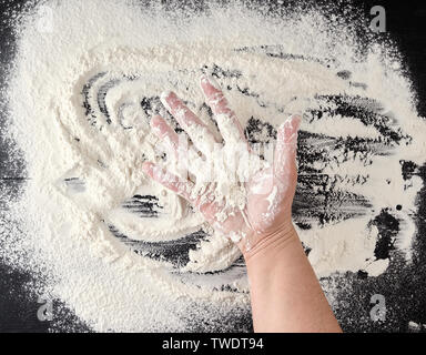 white wheat flour scattered on a black background, product is spread over the surface, kitchen background, top view Stock Photo