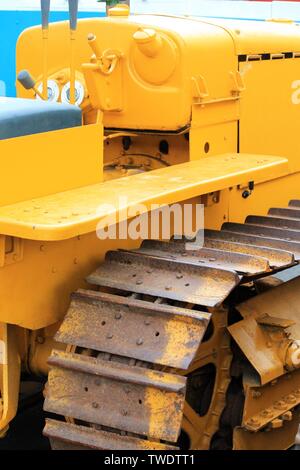 Vertical detail view of a yellow painted restored vintage bulldozer with rusty tracks in an outdoor setting Stock Photo