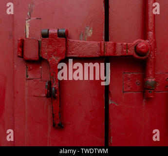 Red industrial rustic metal handles locking two large gate wooden barn style doors. These large doors close off a driveway section in a neighborhood. Stock Photo