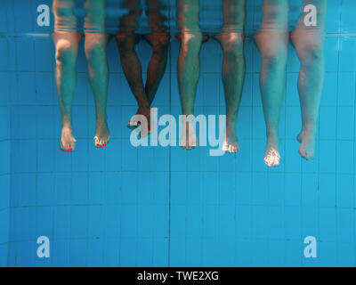 four people legs underwater in the swimming pool. Friends. Party. Summer. Vacation and sport concept. Stock Photo
