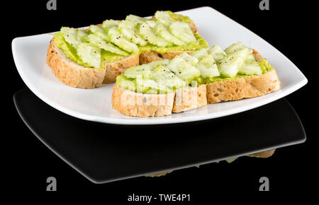 Avocado toasts topped with sliced cucumber with reflection isolated on black background. Studio Shot Stock Photo