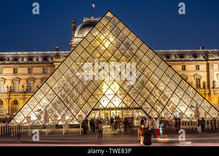 Paris, France, October 04, 2018: The Louvre Palace and the pyramid (by night) as entrance inside Louvre Museum, tourists sightseeing, taking pictures Stock Photo