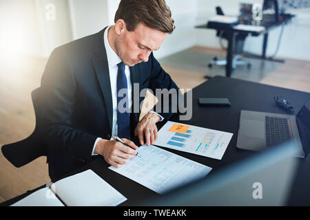 Businessman sitting at his desk in a bright modern office reading paperwork and signing documents Stock Photo