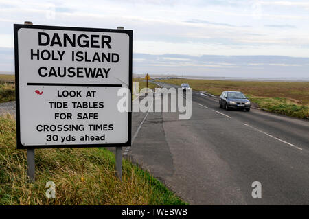 A road warning sign for visiting traffic crossing the 3 mile stretch of a narrow two way tarmac causeway at low tide connecting Lindistfarne Holy Isla Stock Photo