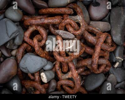 A rusted old chain half buried in pebbles on a beach in Devon, UK Stock Photo