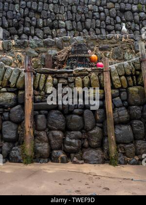 Wooden posts covered in seaweed at a stone walled harbour at low tide in Devon Stock Photo