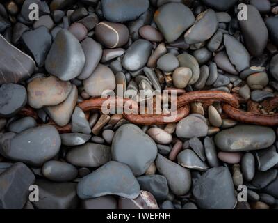 A rusted old chain half buried in pebbles on a beach in Devon, UK Stock Photo