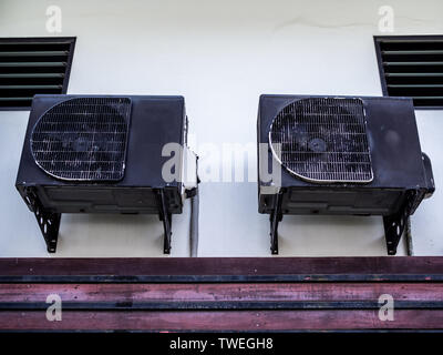 Two old black air conditioner compressors on white wall outside the house. Stock Photo