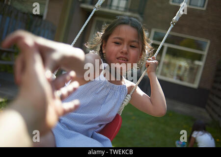 POV of father playing with his young daughter in the back garden on a swing in spring sunshine Stock Photo