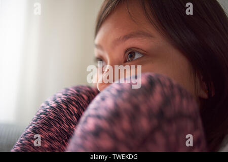 Young Asian girl sitting at home on the sofa with her head between her knees watching television Stock Photo