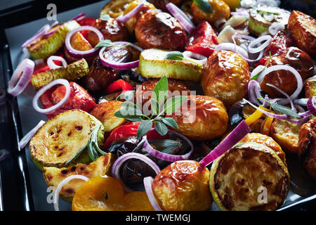 close-up of freshly roasted in an oven hot vegetables  - potatoes, eggplants, zucchini, tomatoes, bell peppers on a baking pan on a grey concrete tabl Stock Photo