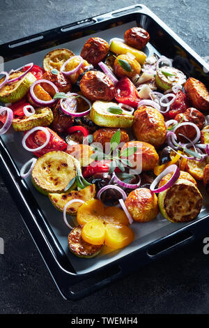 freshly roasted in an oven hot vegetables on a baking pan on a grey concrete table, vertical view from above Stock Photo