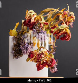 Withered flowers in vase on table on black wall Stock Photo