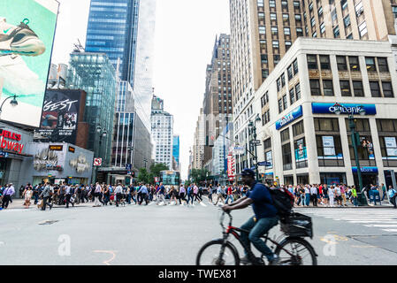 New York City, USA - July 31, 2018: Street with its skyscrapers, traffic, huge advertising screens, cyclist and people around in Manhattan, New York C Stock Photo