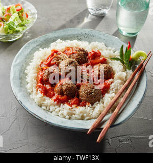 Overhead view on bowl of tasty asian rice with large saucy meatballs and chopsticks on rim of bowl next to water glass Stock Photo