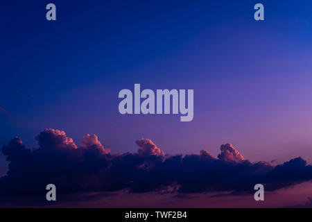 Evening sky at sunset background. Dark clouds hanging above horizon. Majestic cloudscape in blue, orange, violet shades. Grey cloudlets bringing rain. Countryside skyline in twilight time Stock Photo