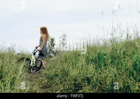 Girl in striped dress riding bike. Spending time outdoors. Child playing outside in spring, summer. Childhood memories. Walking in park, forest. Going on journey, adventure in wilderness Stock Photo